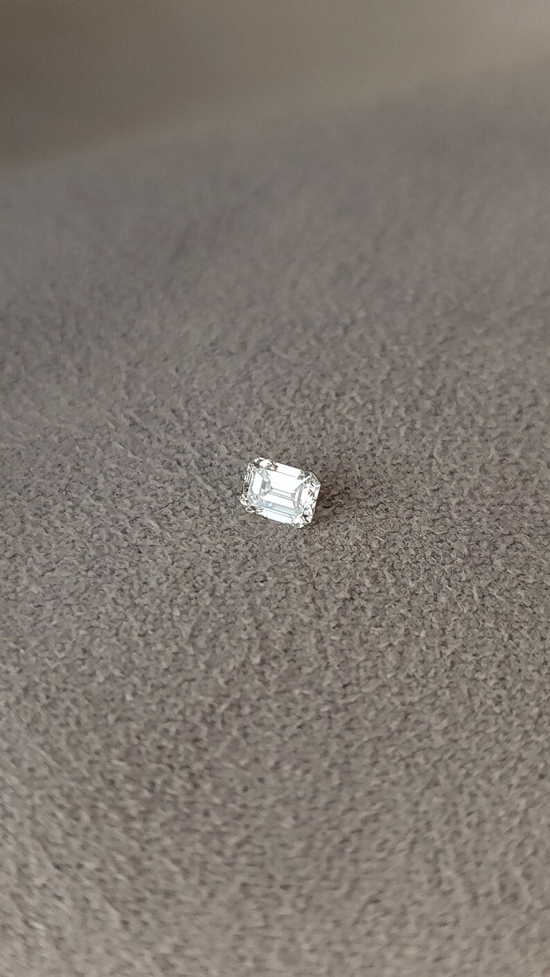 Side view of an emerald cut diamond in tweezers outdoors, focusing on girdle thickness and pavilion depth for secure setting.