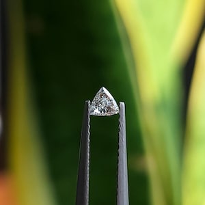 single 3x3mm trillion cut natural diamond held in tweezers side profile against green background, calibrated triangle stone showing crown and pavilion, bright natural daylight reflections, F G VVS VS side stone