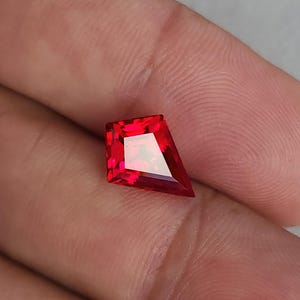 Macro view of the ruby on the palm, showing bold pigeon blood red color and mirror-finish polish. The facets reflect cleanly with no haze, emphasizing flawless clarity. This lab grown synthetic corundum is cut in an angular kite shape that works beautifully in modern bezel rings, east-west pendants, or geometric bridal designs.