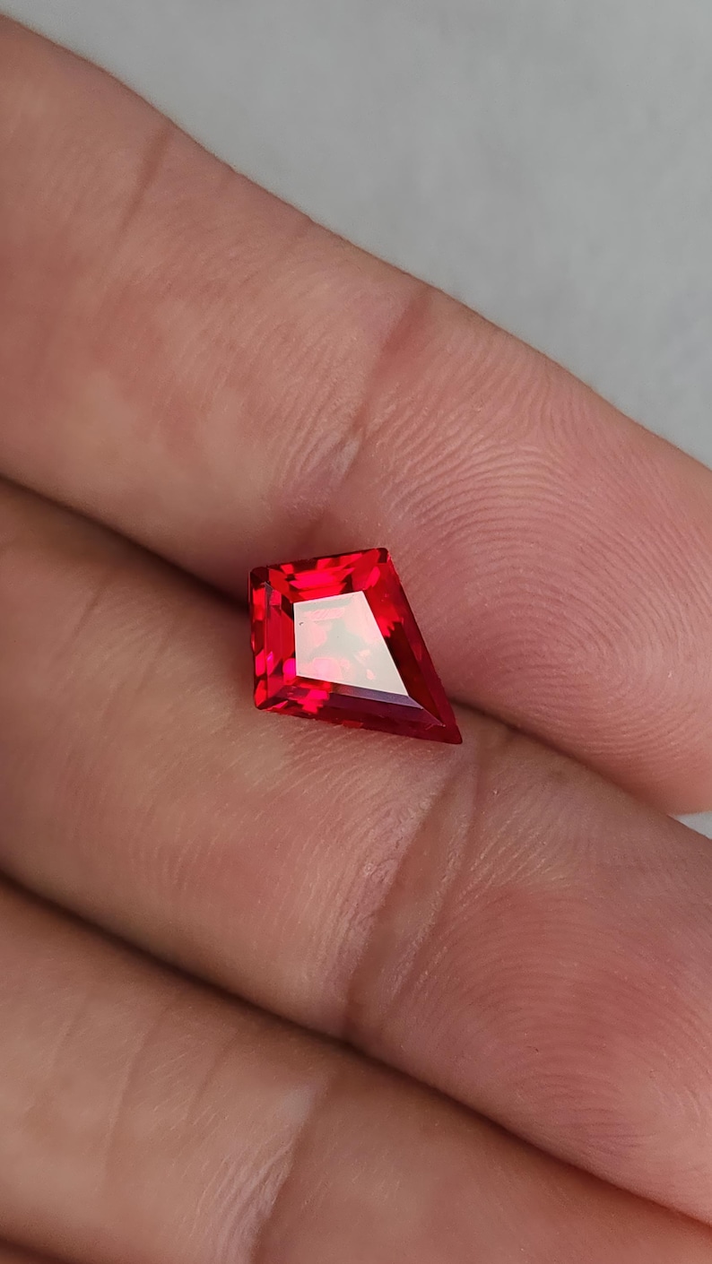 Macro view of the ruby on the palm, showing bold pigeon blood red color and mirror-finish polish. The facets reflect cleanly with no haze, emphasizing flawless clarity. This lab grown synthetic corundum is cut in an angular kite shape that works beautifully in modern bezel rings, east-west pendants, or geometric bridal designs.
