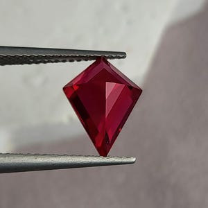 Side tilt of the same precision-cut synthetic ruby in tweezers, showing how the pavilion facets return rich red light. The geometric kite outline feels modern and sculptural, perfect for contemporary high jewelry. With elite AAA grade color, flawless clarity, and expert Thai faceting, this loose ruby is presentation-ready for bespoke commissions.