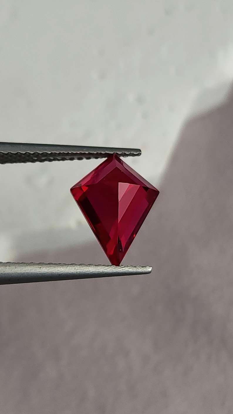 Side tilt of the same precision-cut synthetic ruby in tweezers, showing how the pavilion facets return rich red light. The geometric kite outline feels modern and sculptural, perfect for contemporary high jewelry. With elite AAA grade color, flawless clarity, and expert Thai faceting, this loose ruby is presentation-ready for bespoke commissions.