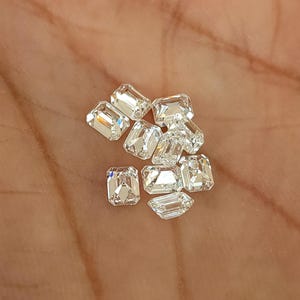 Small cluster of natural emerald cut diamonds on the palm of a hand, showing multiple calibrated 3x2mm and 4x3mm F G SI stones available to buy per piece.