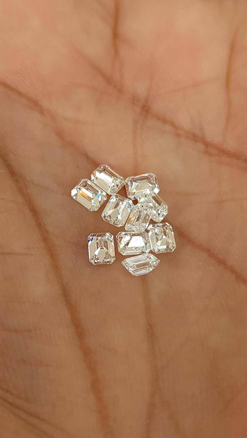 Small cluster of natural emerald cut diamonds on the palm of a hand, showing multiple calibrated 3x2mm and 4x3mm F G SI stones available to buy per piece.