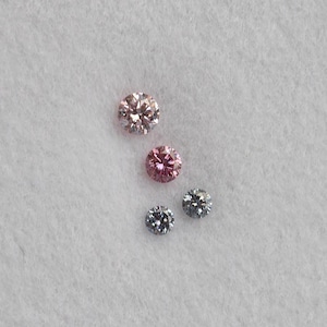 May include: Four round faceted gemstones arranged in a cluster. Two stones are a light pink hue, with the top one being the largest. The remaining two stones are smaller and feature a dark gray, metallic appearance with visible light reflection.