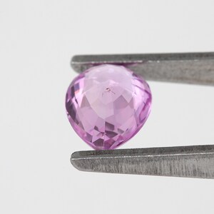 Close tweezers view showing the pear cut unheated natural sapphire from a lower angle, vivid orchid pink color with step like facet reflections, Madagascar natural sapphire highlighted for clarity and cut detail.