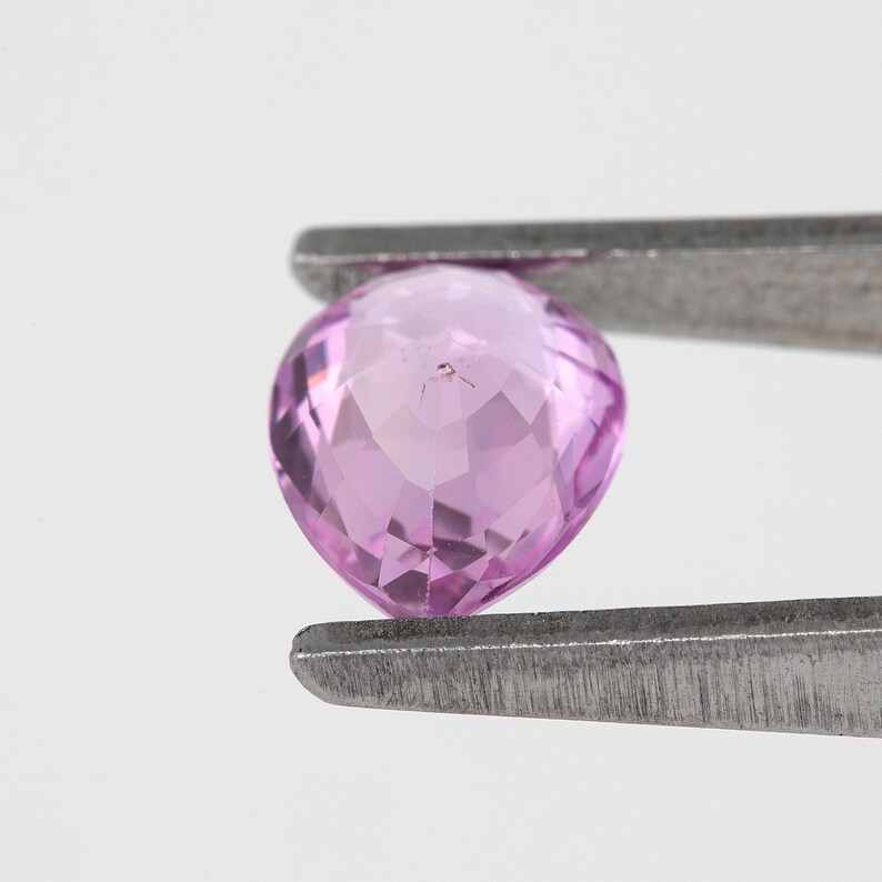 Close tweezers view showing the pear cut unheated natural sapphire from a lower angle, vivid orchid pink color with step like facet reflections, Madagascar natural sapphire highlighted for clarity and cut detail.