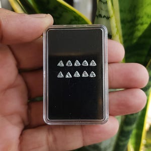 handheld case with multiple 3x3mm trillion cut natural diamonds shown outdoors near greenery, calibrated triangle side stones for halos and bands, F G near colorless VVS VS, trade jewelry supply photo