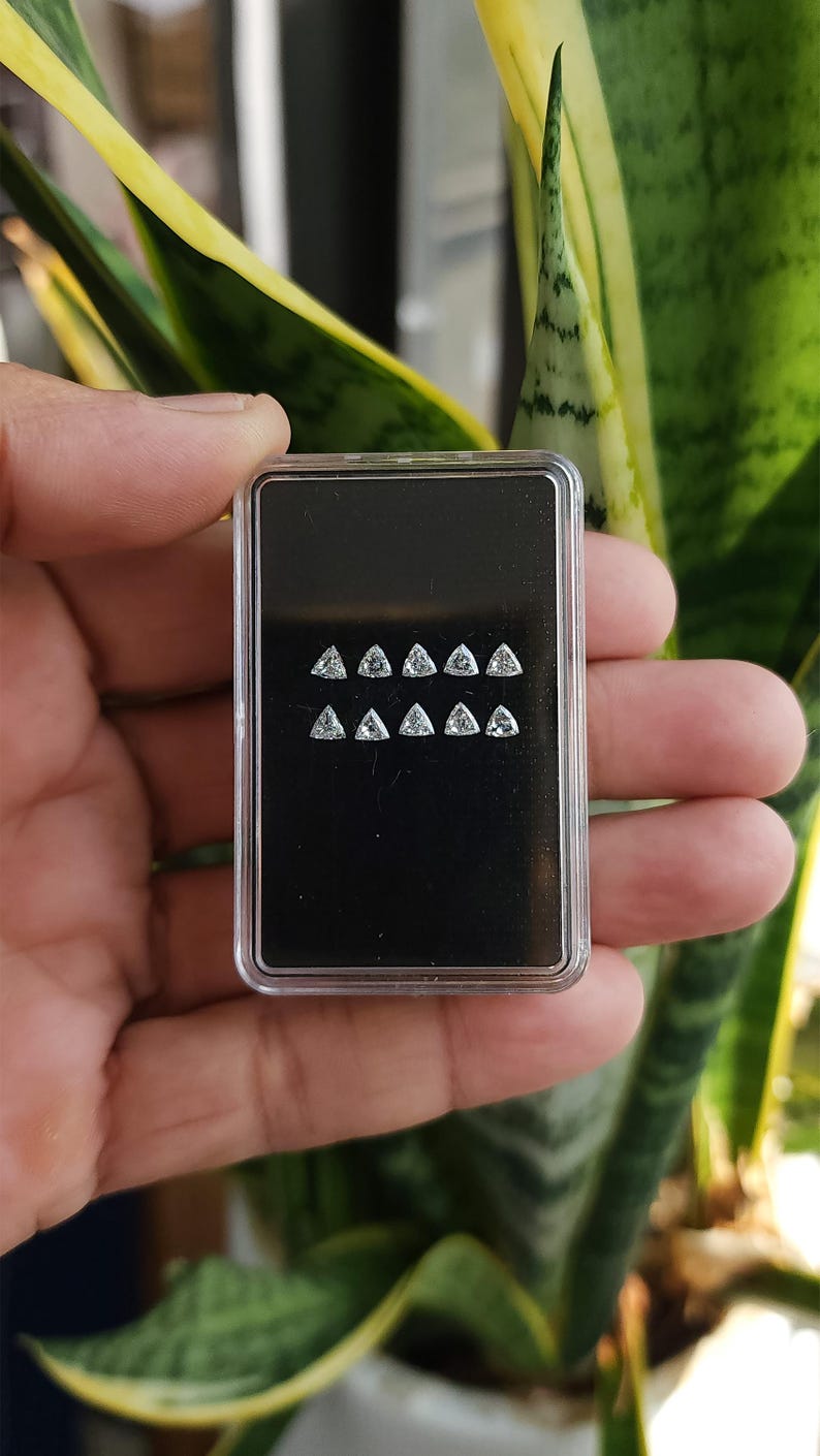 handheld case with multiple 3x3mm trillion cut natural diamonds shown outdoors near greenery, calibrated triangle side stones for halos and bands, F G near colorless VVS VS, trade jewelry supply photo