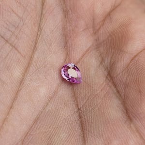 Palm scale photo of the pear cut unheated natural sapphire, vivid orchid pink sparkle in ambient light, compact size and bright brilliance, Madagascar loose sapphire for ring or pendant.