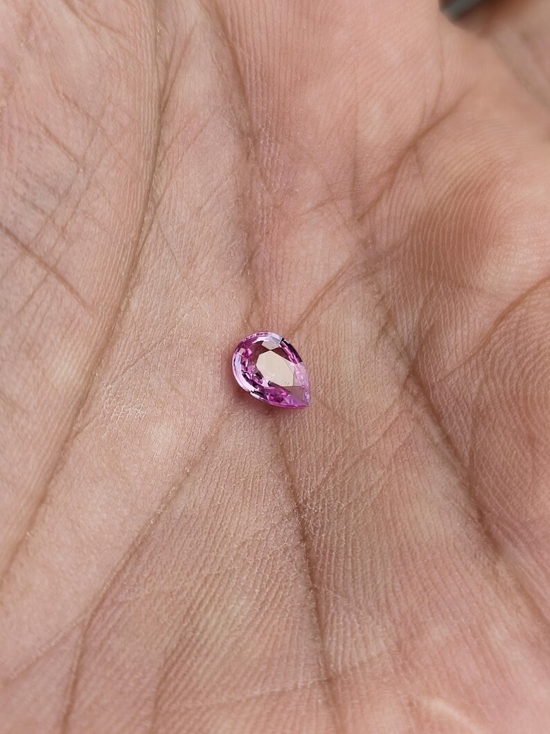 Palm scale photo of the pear cut unheated natural sapphire, vivid orchid pink sparkle in ambient light, compact size and bright brilliance, Madagascar loose sapphire for ring or pendant.