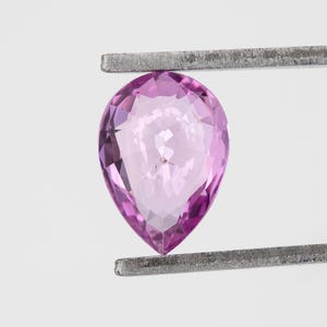 Face up tweezers photo of the pear cut unheated natural sapphire, vivid orchid pink saturation with crisp facet junctions, strong light return around the edges, Madagascar loose sapphire shown for cut symmetry.