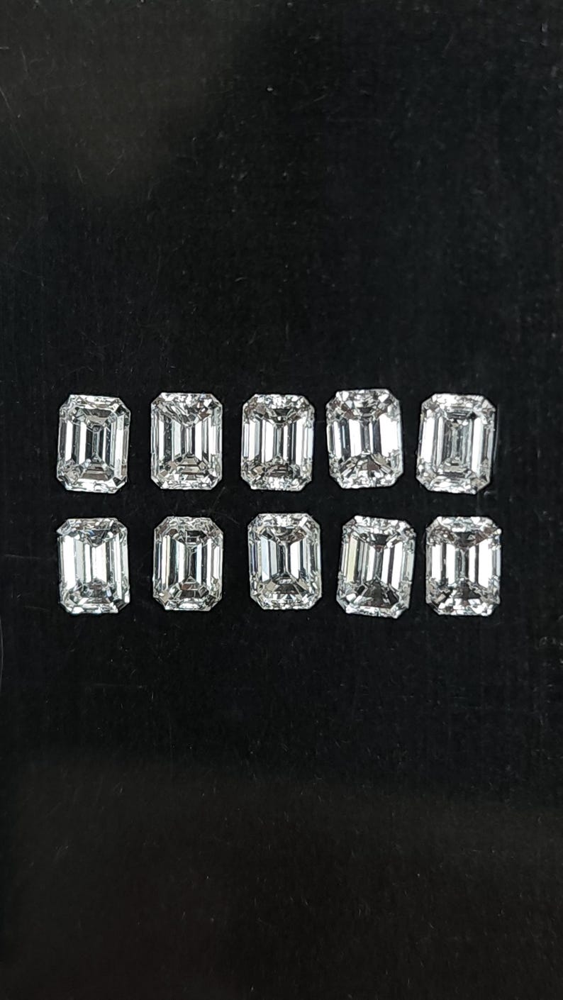 Group of ten natural emerald cut diamonds arranged in two rows on a black background, calibrated 3x2mm and 4x3mm F G SI side stones for rings and fine jewelry.