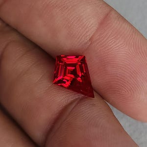 Close-up of the same kite cut ruby resting on skin at a slight angle, catching internal neon red fire. This photo highlights face-up brilliance and crisp facet junctions from expert Thai cutting. The stone is AAA grade, flawless clarity, and sold loose for custom jewelry orders, including unique engagement rings and luxury pendants.