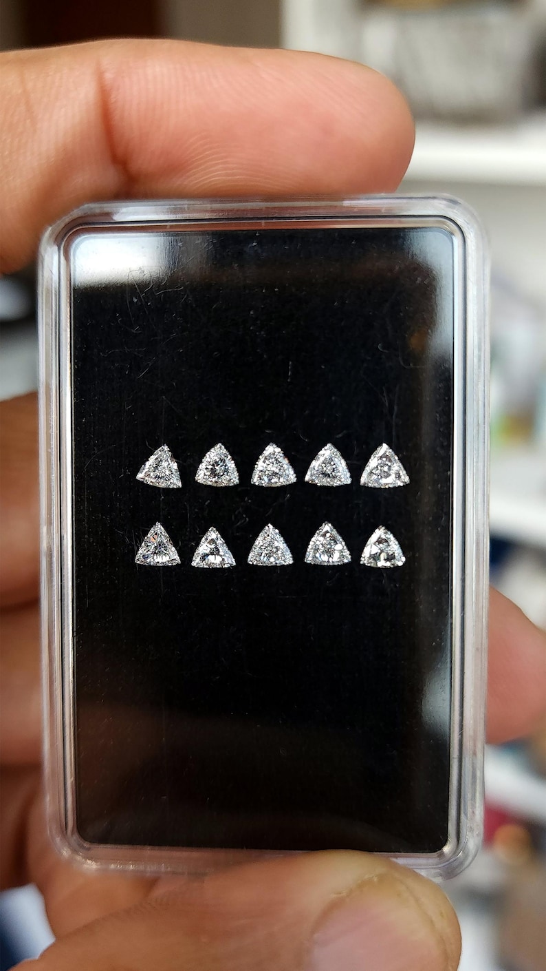 3x3mm trillion cut natural diamond side stones shown on a black display card inside a small case, calibrated triangle diamonds for halo and three stone ring layouts, F G color VVS VS clarity, natural daylight photo