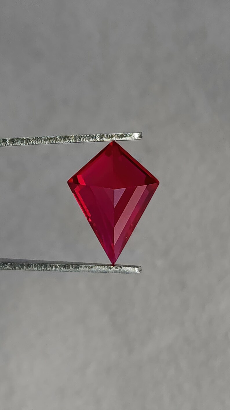 Reverse view of the lab created ruby in tweezers, showing the pavilion architecture and clean facet alignment of the kite cut. The stone displays intense red without brown or pink shift. Flawless clarity and elite polish make it suitable for luxury bridal jewelry, heirloom reinterpretations, or custom orders where exact size and shape matter.
