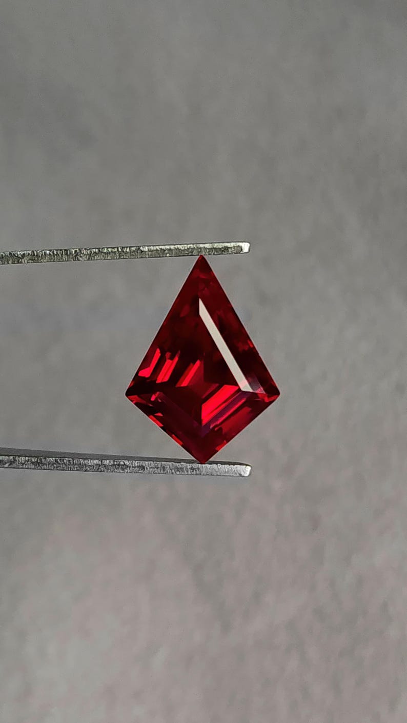 Close-up tweezers view of the lab grown ruby face-up, tilted to capture the saturated pigeon blood red tone that buyers look for in high luxury ruby jewelry. The symmetrical kite cut and sharp facet junctions come from expert Thai cutting and polishing. Flawless clarity and top AAA grade quality make it perfect as a designer center stone.