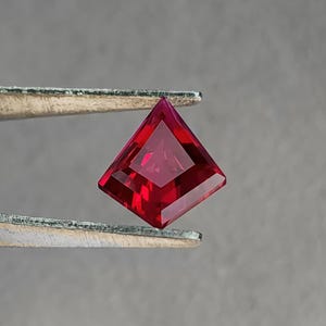 Face-up view of the same ruby in tweezers, showing even color saturation across the entire stone with no windowing. The vivid red hue and flawless clarity imitate the look of elite Burmese-style “pigeon blood” material. Precision Thai faceting gives crisp symmetry, making this loose ruby perfect for collectors or bespoke fine jewelry projects.