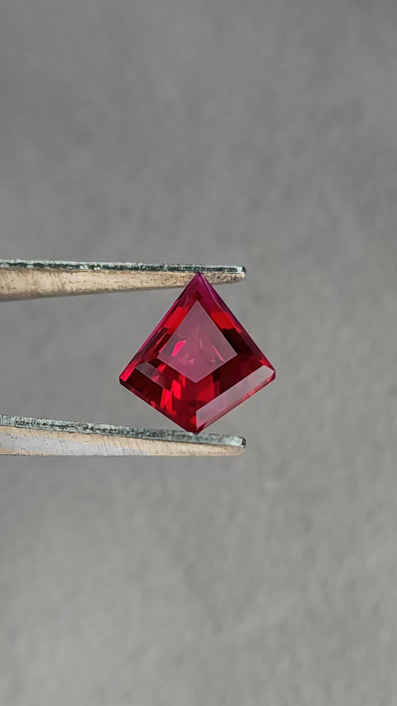 Face-up view of the same ruby in tweezers, showing even color saturation across the entire stone with no windowing. The vivid red hue and flawless clarity imitate the look of elite Burmese-style “pigeon blood” material. Precision Thai faceting gives crisp symmetry, making this loose ruby perfect for collectors or bespoke fine jewelry projects.