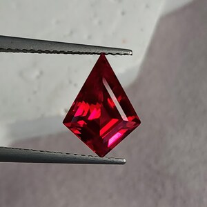 Three-quarter angled shot of the ruby in tweezers, lit to show internal glow and mirror-finish polishing. The gem’s intense red tone and sharp facet junctions highlight master Thai cutting. This loose AAA grade lab grown ruby is ideal for a designer ring center stone, a one-off pendant, or upscale bridal jewelry that needs bold color.