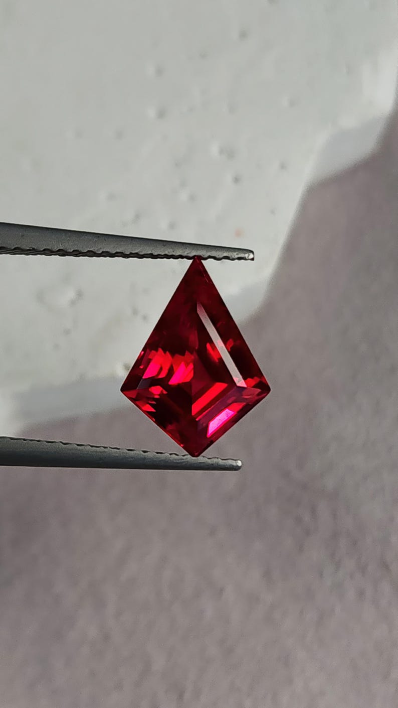 Three-quarter angled shot of the ruby in tweezers, lit to show internal glow and mirror-finish polishing. The gem’s intense red tone and sharp facet junctions highlight master Thai cutting. This loose AAA grade lab grown ruby is ideal for a designer ring center stone, a one-off pendant, or upscale bridal jewelry that needs bold color.