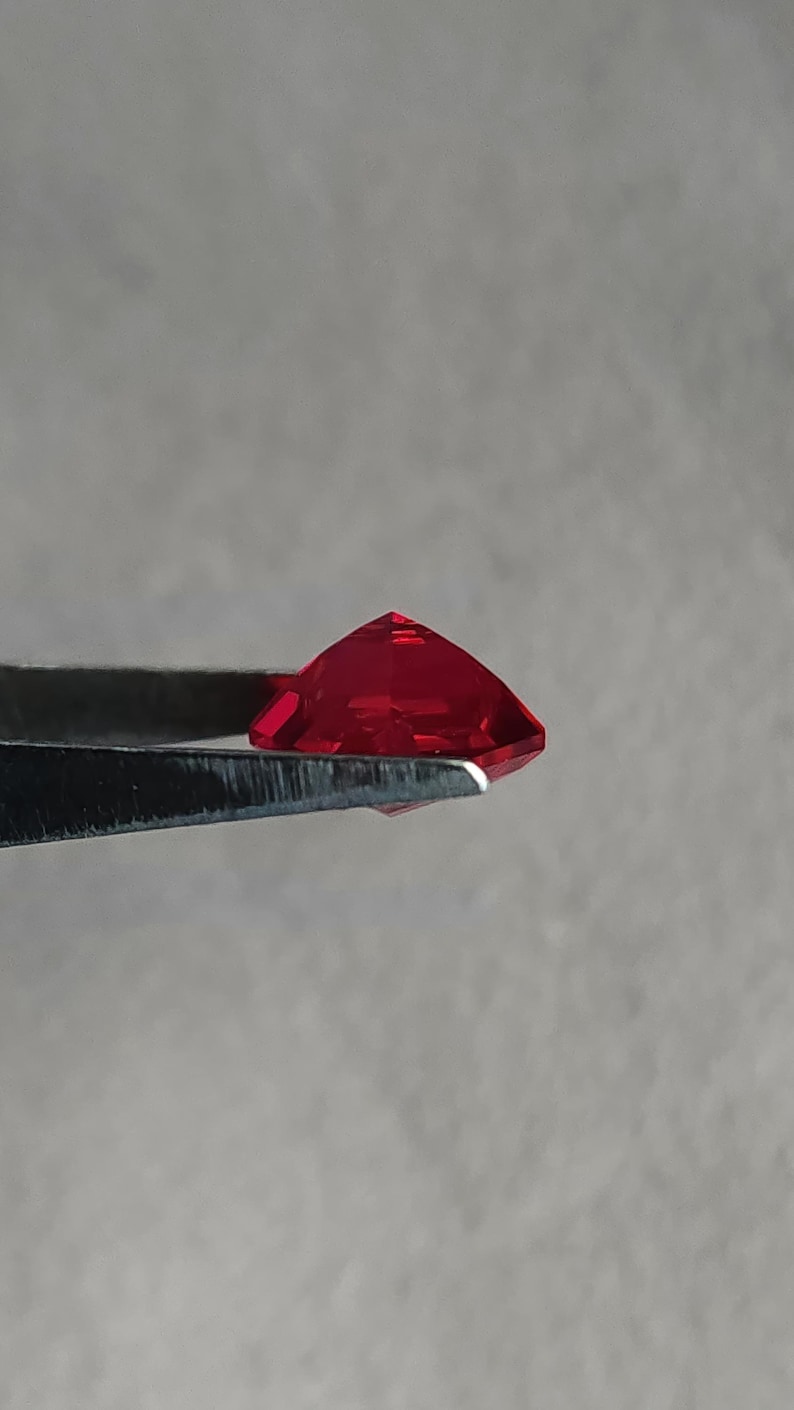 Profile shot of the precision-cut kite shape lab created ruby held in tweezers, showing pavilion depth and clean girdle. The stone glows intense pigeon blood red with zero visible inclusions, proof of flawless clarity. This custom-cut AAA grade ruby is calibrated for high-end rings, pendants, and bespoke settings where you want bold color without natural ruby pricing.