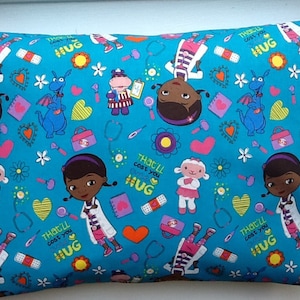 May include: A rectangular pillow with a teal background featuring cartoon characters, hearts, flowers, and medical-themed icons. The pillow has the text "That'll cost you HUG" printed on it. The pillow is designed for children.
