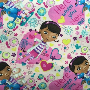 May include: Fabric featuring a repeating pattern of a cartoon girl, a blue dragon, and a lamb. The design includes pink hearts, flowers, and the text "Here when you Need me". The color palette is primarily pink, white, and blue.