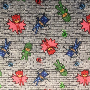 May include: Fabric featuring a repeating pattern of cartoon characters in red, green, and blue, set against a gray brick wall background. The characters have superhero-like costumes and poses, with some appearing upside down.