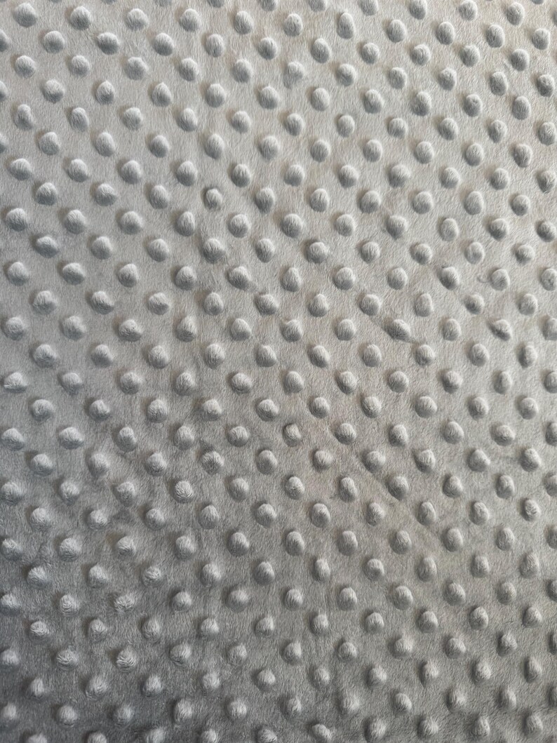 May include: Close-up of a soft, gray fabric with a textured surface. The fabric is covered in evenly spaced, raised, rounded bumps, creating a tactile and visually interesting pattern. The material appears plush and comfortable, suitable for blankets or other cozy items.