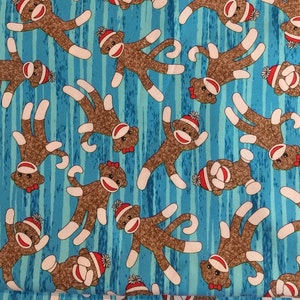 May include: A blue fabric with a repeating pattern of brown sock monkeys wearing red and white knit hats. The monkeys have white arms and legs and are in various poses.