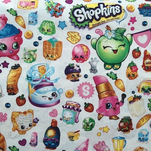 May include: White fabric featuring a colorful pattern of Shopkins characters. The design includes various food-themed characters like cupcakes, apples, and lipsticks, along with the Shopkins logo. The fabric is covered with cartoon-style illustrations.