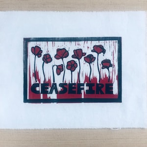 May include: A black framed print with a red background and a black and white illustration of red poppies. The text "CEASEFIRE" is printed in black letters at the bottom of the print.
