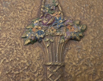 Puede incluir: Una superficie dorada texturizada con un diseño en relieve de una cesta llena de flores. La cesta tiene una base tejida y un asa, mientras que el arreglo floral incluye detalles pintados en tonos azul, naranja y verde.