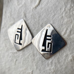 May include: A pair of silver earrings with a geometric design. The earrings are shaped like diamonds and have a cutout design in the center.