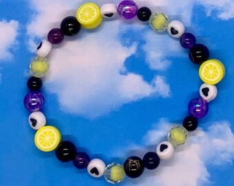 May include: A colorful beaded bracelet with purple, black, white, and yellow beads. Some of the beads are shaped like lemons and hearts.