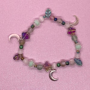 May include: A delicate bracelet with a moon and leaf charm, featuring pink, green, and purple beads.