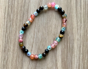 May include: A multi-coloured gemstone bead bracelet. The bracelet features a variety of beads in shades of black, pink, blue, orange, and green. The beads are strung on an elastic cord, forming a circular shape.