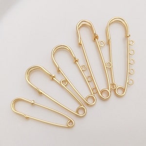 May include: Five gold safety pins of varying lengths, each with multiple loops at the top.