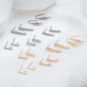 Puede incluir: Una colección de hallazgos para pendientes de oro y plata, incluyendo ganchos, postes y bucles. Los hallazgos están dispuestos sobre una superficie blanca. Acero inoxidable.