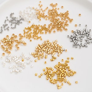 Puede incluir: Surtido de pequeños anillos de salto de metal en oro, plata y una mezcla de oro y plata. Los anillos de salto están esparcidos sobre una superficie blanca.