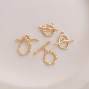 以下が含まれることがあります： さまざまなデザインの、金色のトグルクラスプが4つ。バーとリングまたは楕円形の形状で、テクスチャ加工された有機的な外観です。ジュエリー作りに最適で、ネックレスやブレスレットをしっかりと留めることができます。