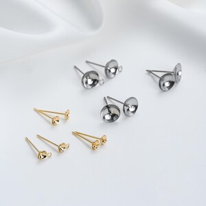 May include: A set of earring findings in gold and silver tones. The findings are made of metal and have a small loop at the top for attaching earrings. The findings are shown on a white background.