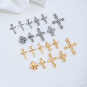 Può includere: Una collezione di piccoli ciondoli in metallo con vari design a croce e forme di quadrifoglio in tonalità argento e oro. Ogni ciondolo include un piccolo anello sulla parte superiore per l'aggancio, con dettagli intricati e croci di diverse dimensioni.