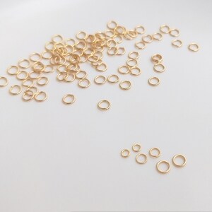 May include: A large quantity of gold jump rings of various sizes, scattered on a white surface.