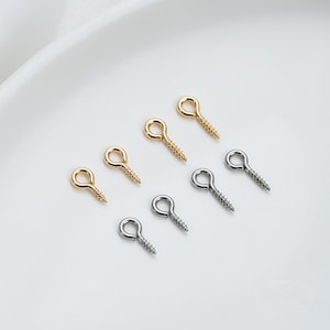 Può includere: Un set di otto occhielli a vite in tonalità oro e argento. Gli occhielli sono piccoli e hanno un anello arrotondato nella parte superiore e una filettatura a vite nella parte inferiore.