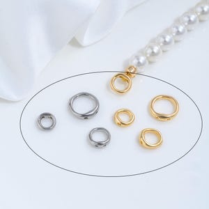 Puede incluir: Un surtido de pequeños hallazgos de joyería redondos en tonos plateados y dorados. Los hallazgos son de varios tamaños y formas, con una hebra de perlas en el fondo. Los hallazgos probablemente se utilizan para la fabricación de joyas.