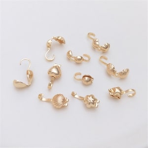 Op de afbeelding: Assortiment van goudkleurige metalen sluitingen voor het maken van sieraden. De sluitingen zijn in verschillende vormen, waaronder hart, schelp, bloem en cirkel.