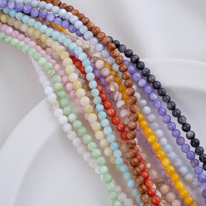 May include: Assortment of colorful round beads made from natural materials. The beads are strung on a white surface and are arranged in a rainbow pattern.