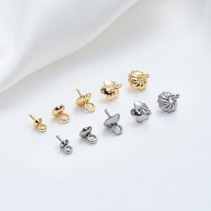 May include: Assortment of gold and silver metal bead caps with different shapes and sizes. The bead caps have a loop on one end and a pointed end on the other.